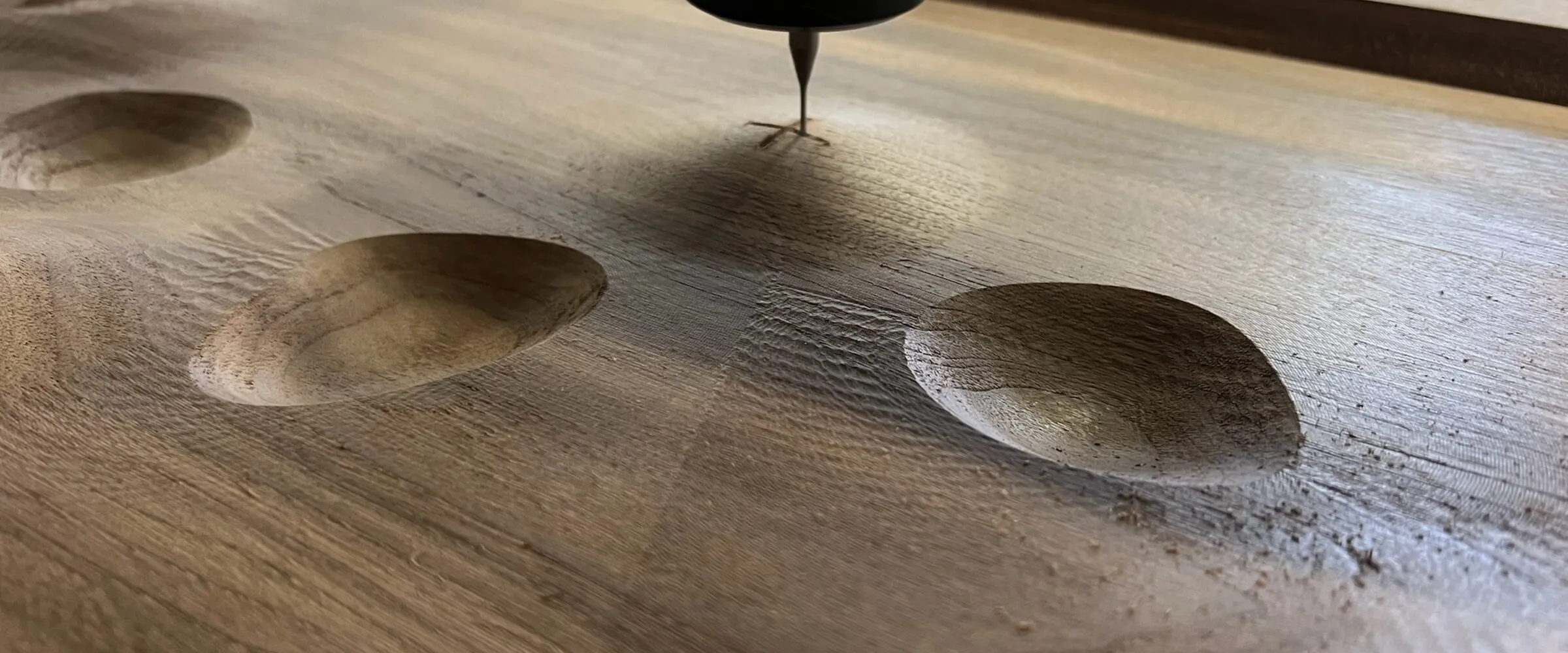 A CNC router cutting dished pockets into a walnut panel